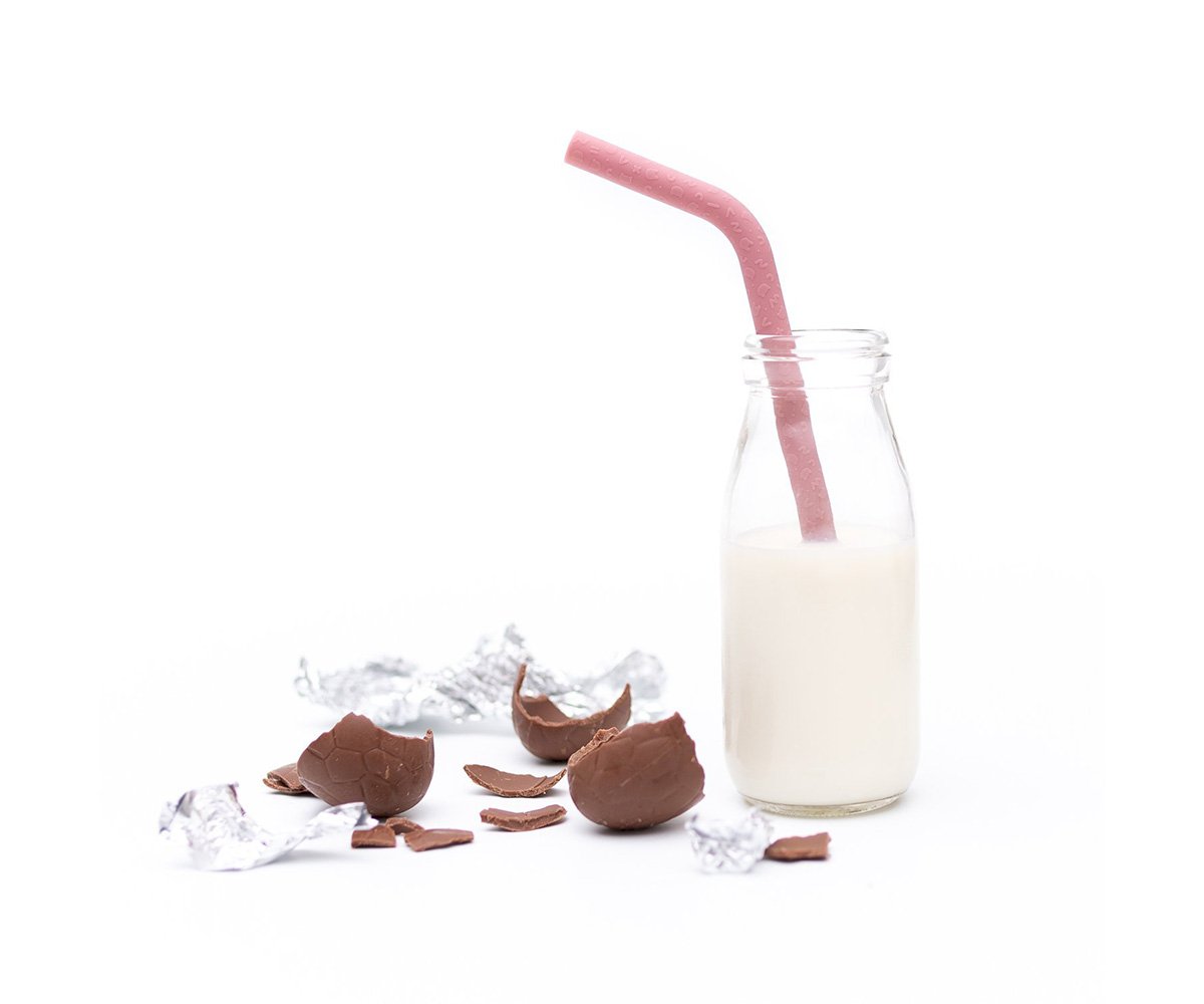 Palhinha de silicone Bendie Straws rosa inserida numa garrafa de leite, com ovos de chocolate partidos à volta, sugerindo um lanche divertido.