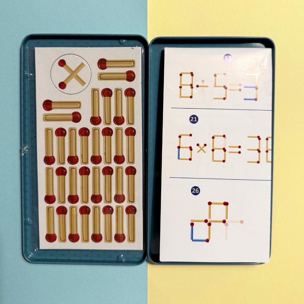 Interior da caixa do jogo de fósforos magnéticos, exibindo o conjunto de varetas magnéticas numa secção e cartões com desafios matemáticos e de formas na outra.
