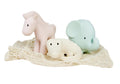 Conjunto de três mordedores de borracha natural da Tikiri (cavalo rosa, elefante azul-claro e crocodilo branco) pousados sobre uma rede de algodão.