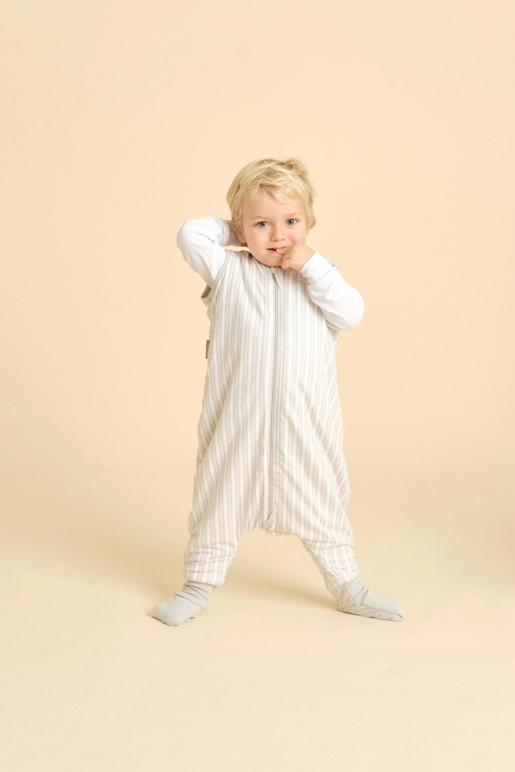 Criança loira de pé, a usar o saco de dormir MolisandCo TOG 1.0 Dawn Stripes com pés e meias, demonstrando liberdade de movimentos.