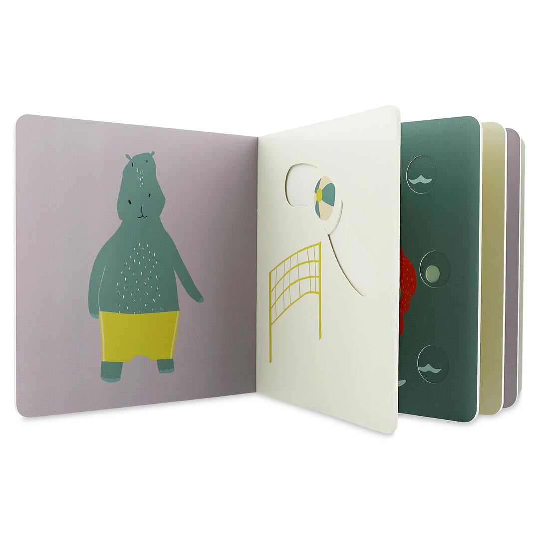 Livro Trixie aberto, mostrando o interior com ilustrações de um hipopótamo de calções de banho e uma cena de voleibol de praia com rede.