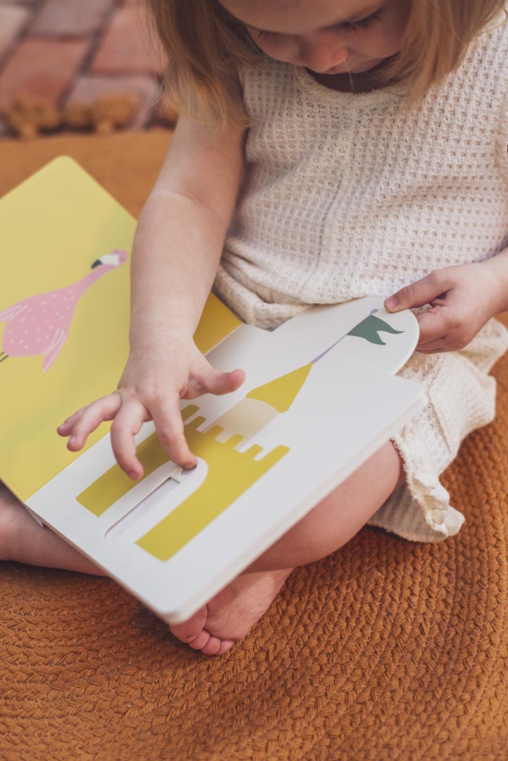 Foco nas mãos de uma criança a interagir com o mecanismo de deslizar de uma página que mostra um castelo de areia.