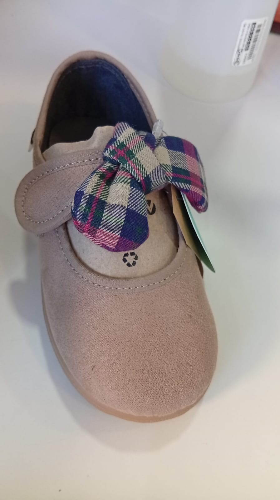 Vista frontal do Victoria Sapato com laço em camurça Bege, destacando a textura suave, a tira de velcro e o laço xadrez.