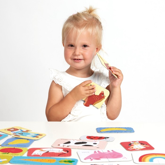 Uma menina sorridente a segurar orgulhosamente o puzzle de um cavalo que acabou de montar, do conjunto Banana Panda First Words.