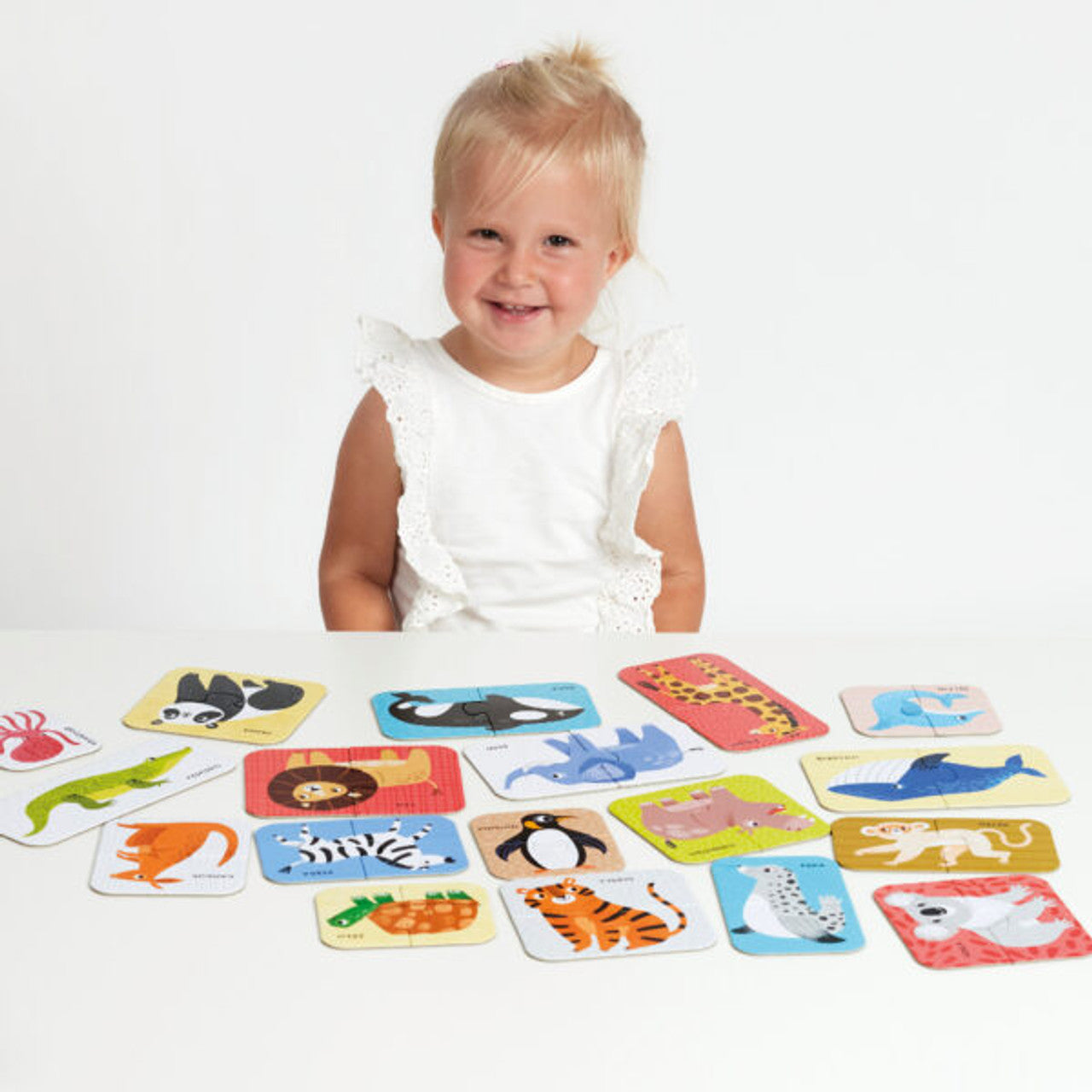 Uma criança sorridente a brincar com as peças do puzzle Banana Panda Puzzle Pairs - Animais Selvagens numa mesa branca.