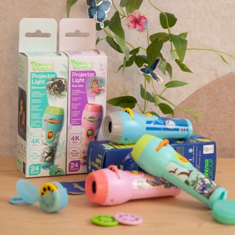 Conjunto de projetores de luz Natural Creation (dinossauros e jardim) com as respetivas caixas e discos de projeção sobre uma superfície, com decoração floral ao fundo.