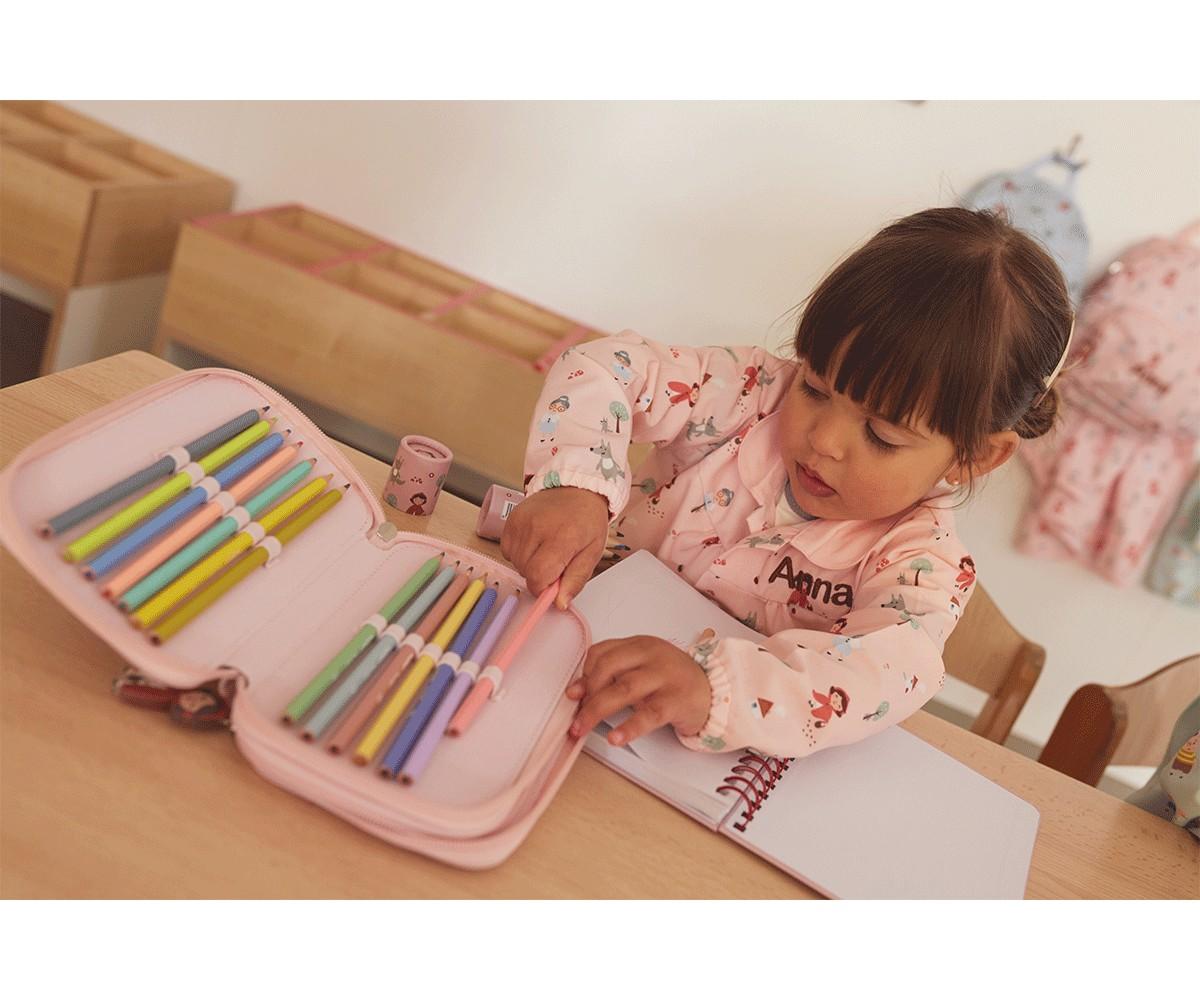 Criança a escolher um lápis de cor de um estojo rosa, sentada numa secretária com um Caderno Escolar Tutete aberto.