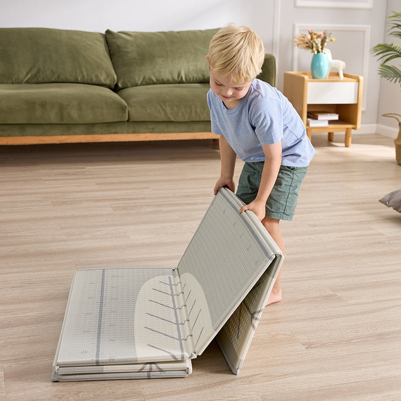 Criança a dobrar facilmente o Hape Tapete Dobrável, mostrando a sua portabilidade e como é compacto para arrumação.
