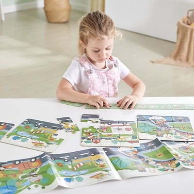 Uma menina concentrada a montar uma das cenas do Hape Puzzle Veículos de Resgate numa mesa branca, com o poster guia ao lado.