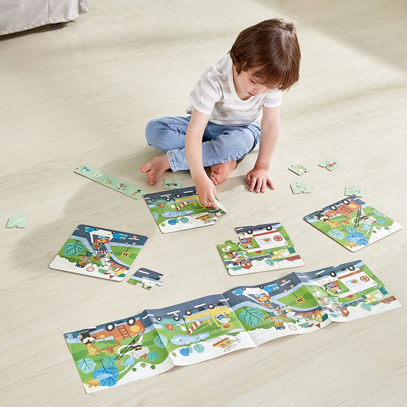 Um menino sentado no chão a brincar com as várias peças e puzzles do conjunto Hape Veículos de Resgate, demonstrando a diversão.