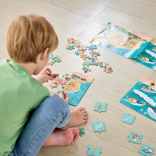 Criança a montar uma das secções do Hape Puzzle 3 em 1 Oceano no chão, com peças espalhadas e outras partes do puzzle.