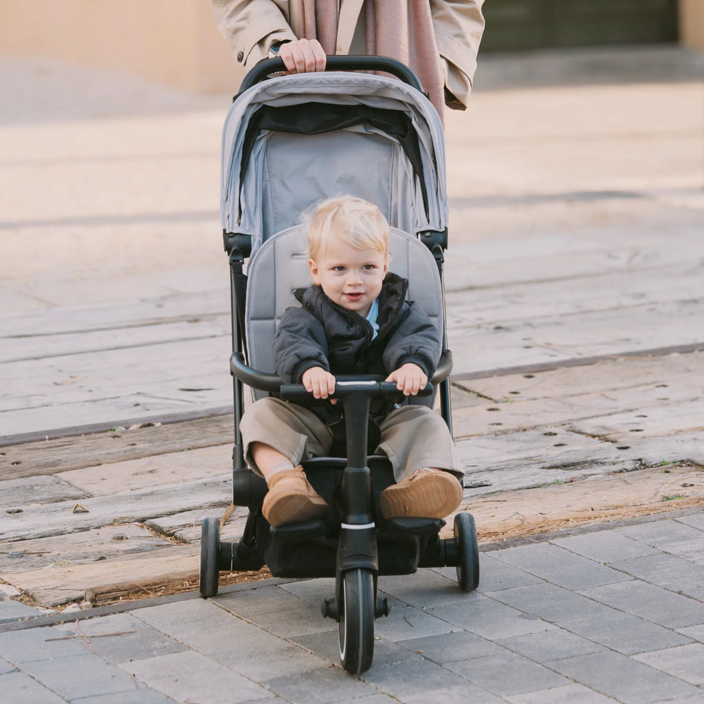 Criança sentada no Smartrike Traveler em modo triciclo, com controlo parental, a passear em terreno exterior.