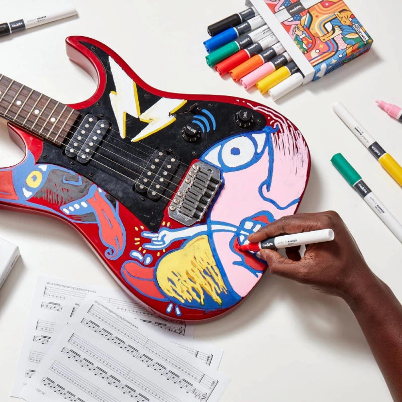 Pessoa a pintar uma guitarra elétrica vermelha com um marcador acrílico Carioca Plus, mostrando a versatilidade do produto em superfícies diversas.