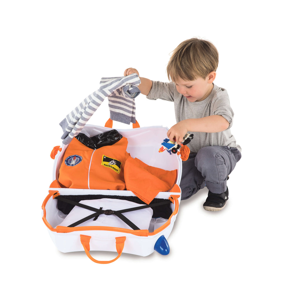 Menino a arrumar a sua mala Trunki branca e laranja, colocando um fato de astronauta e brinquedos no seu interior.