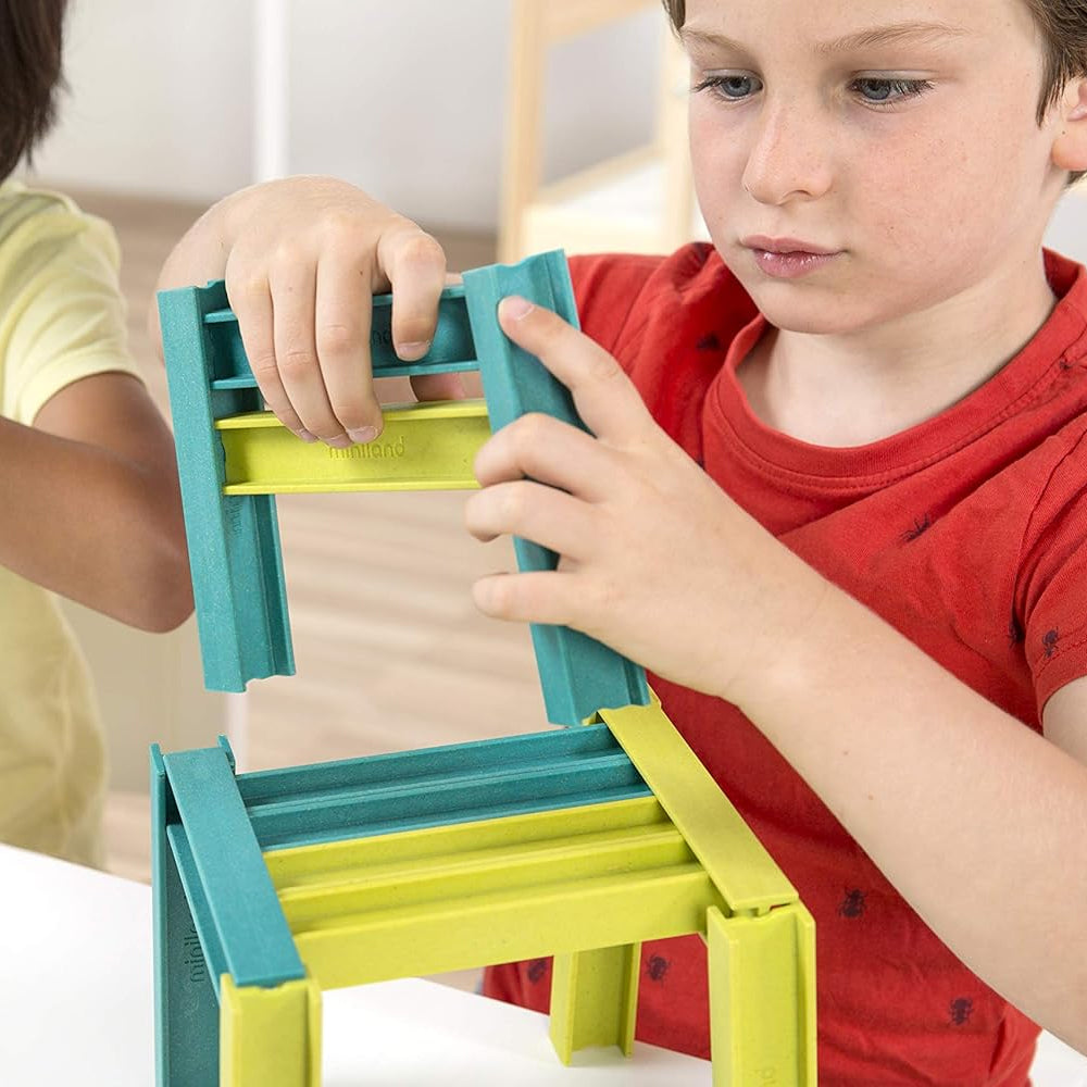 Detalhe das mãos de uma criança a encaixar com precisão as vigas de construção Miniland Eco Beams, desenvolvendo a motricidade fina.