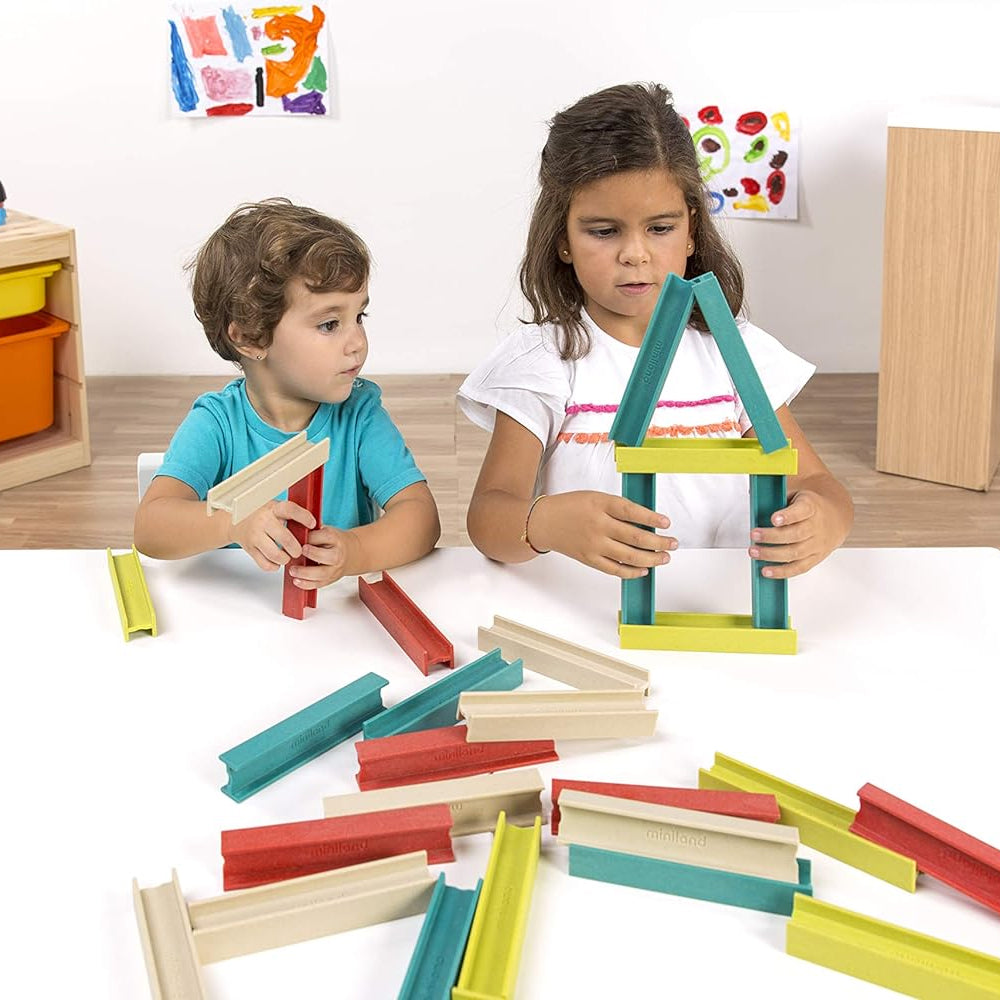 Crianças a colaborar numa mesa de atividades, a montar estruturas com as vigas coloridas do brinquedo educativo Miniland Eco Beams.