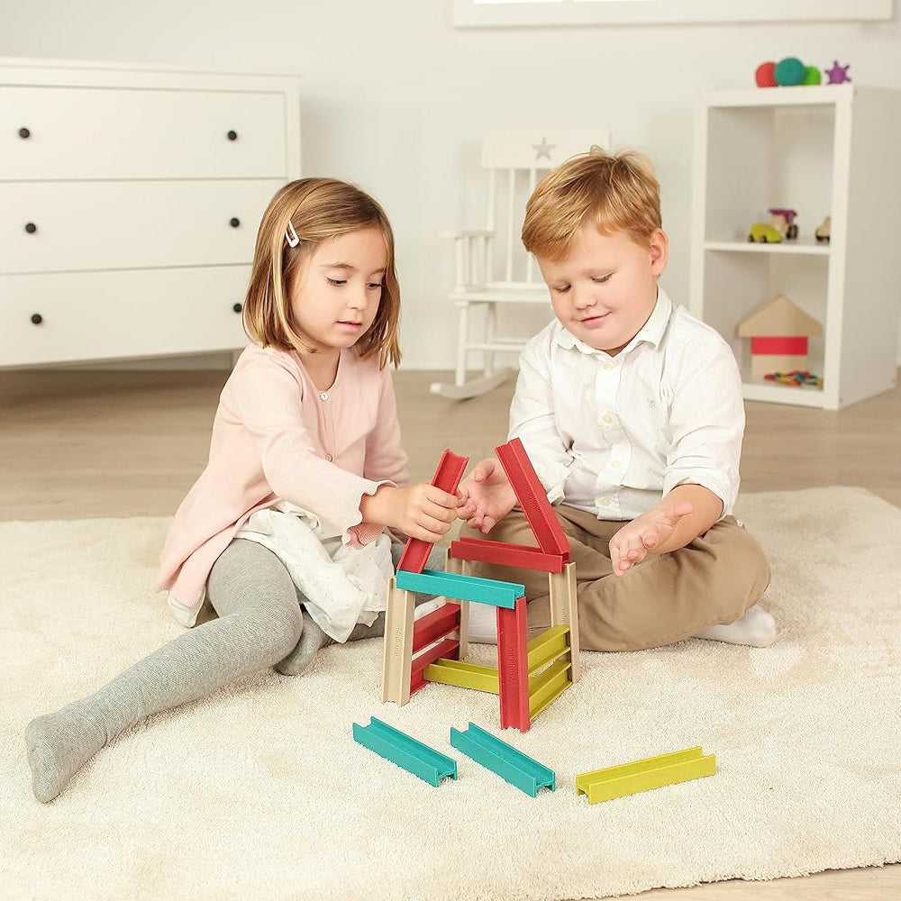Duas crianças a brincar no chão da sala, construindo uma casa com o set de construção ecológico Miniland Eco Beams de 32 peças.