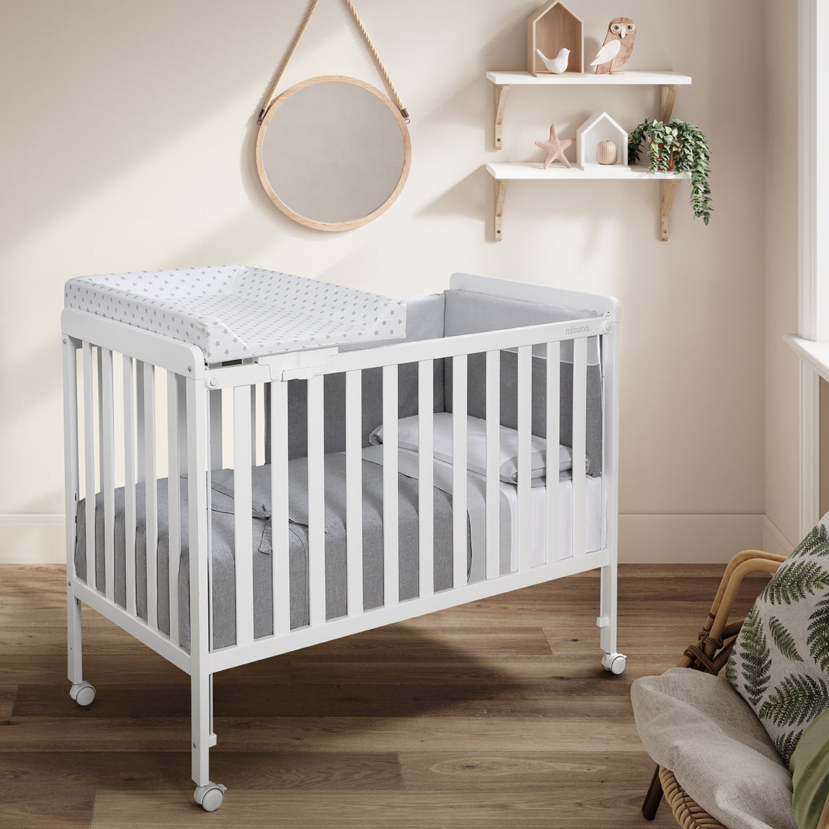 Berço Micuna branco com trocador de berço Micuna 120x60 com padrão de estrelas cinza, integrado num quarto de bebé.