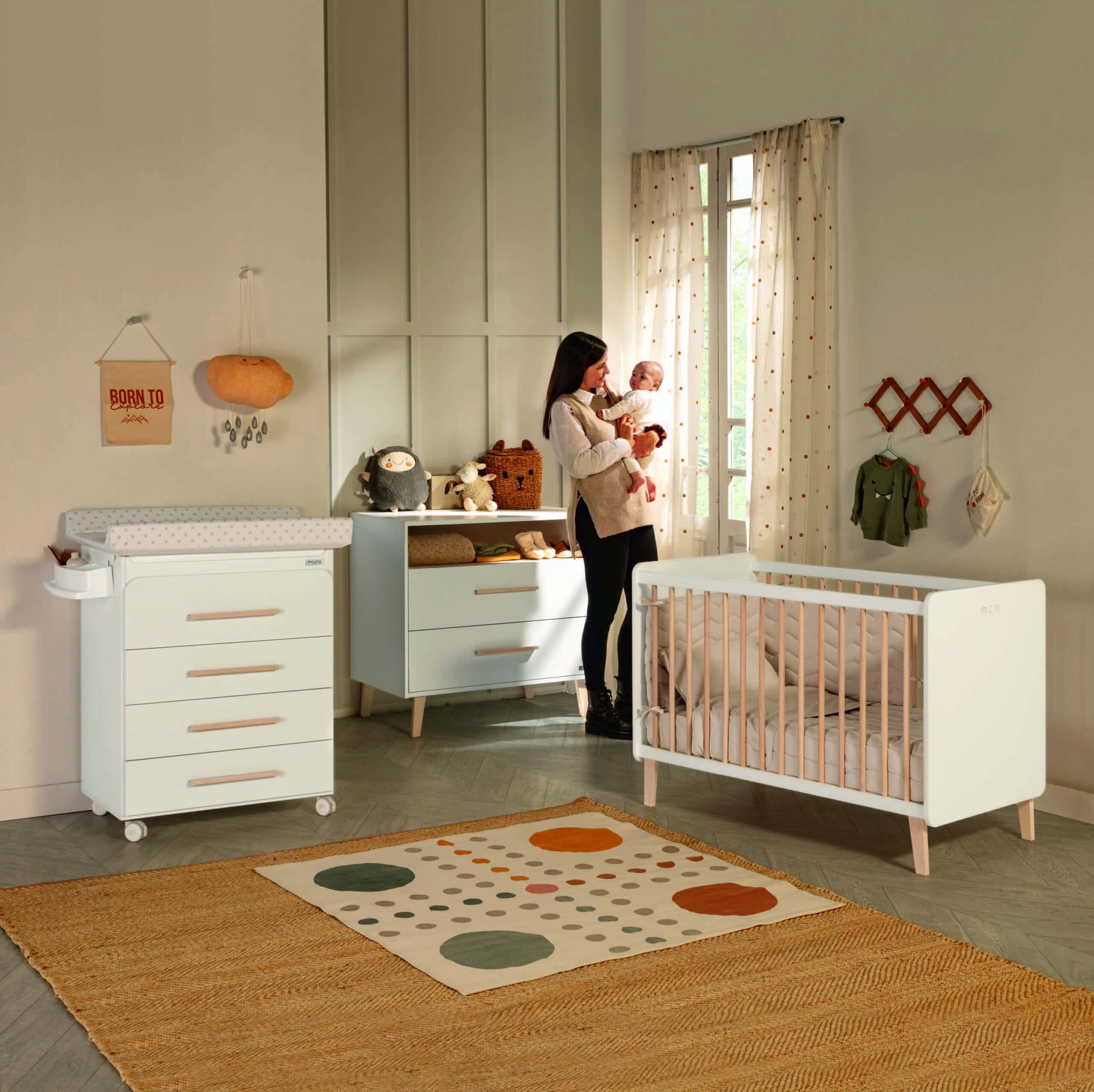 Mãe com bebé ao colo em quarto de bebé, com o berço Micuna Trevi 120x60 e cómoda.
