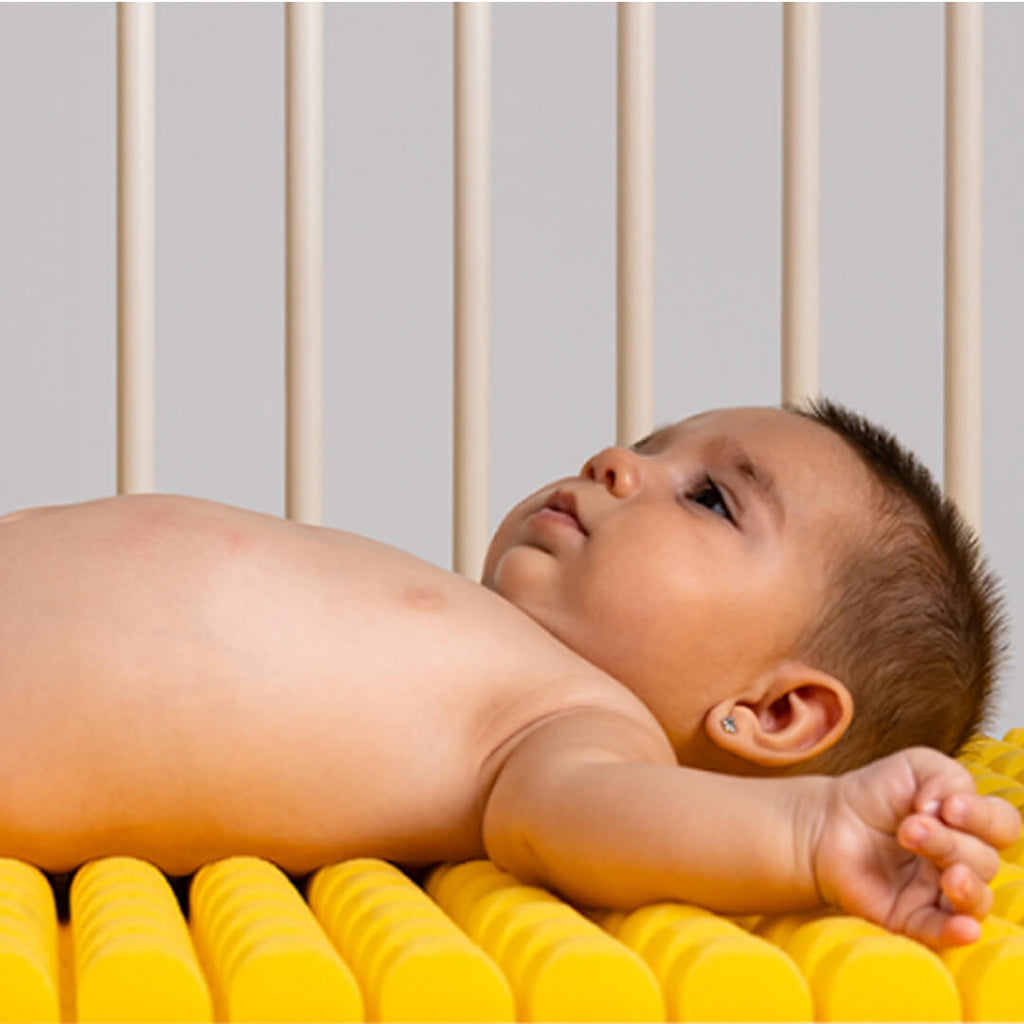 Bebé deitado confortavelmente no colchão Micuna premium HR Perfilado amarelo, mostrando o design ergonómico e a textura perfilada.