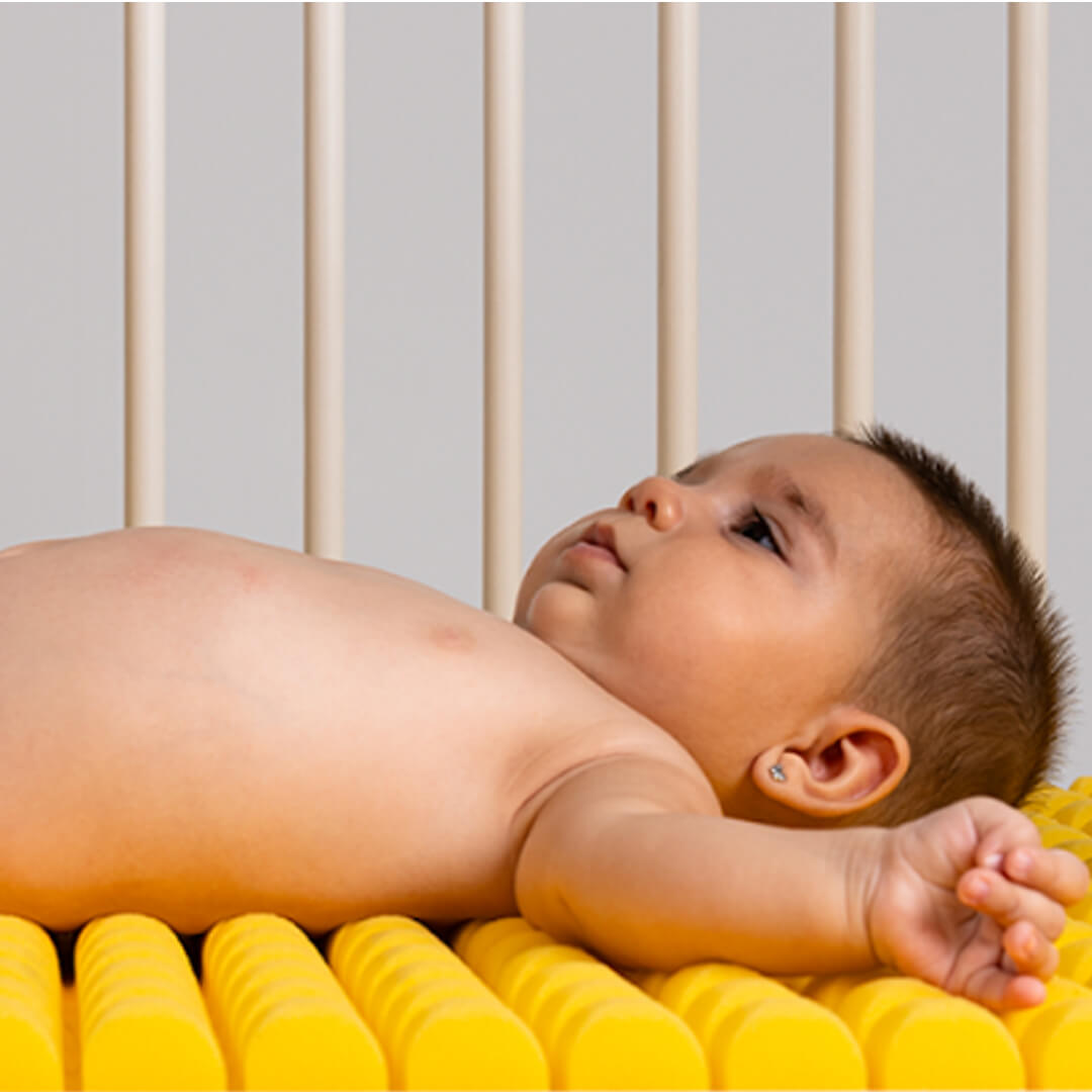 Bebé deitado confortavelmente no colchão Micuna premium HR Perfilado amarelo, mostrando o design ergonómico e a textura perfilada.