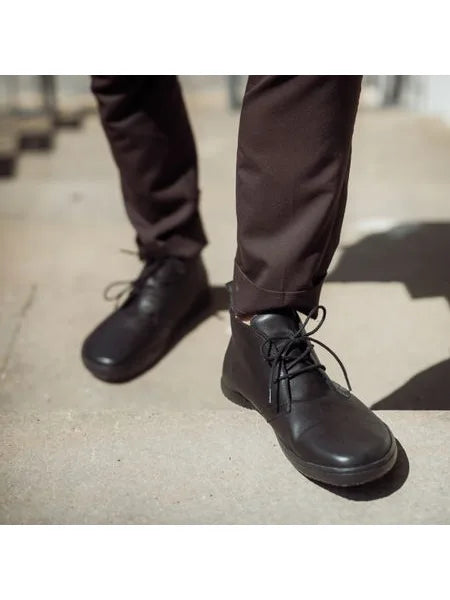 Pés de uma pessoa a usar os sapatos barefoot pretos Angles Atlas em escadas de cimento, demonstrando o uso casual e elegante.