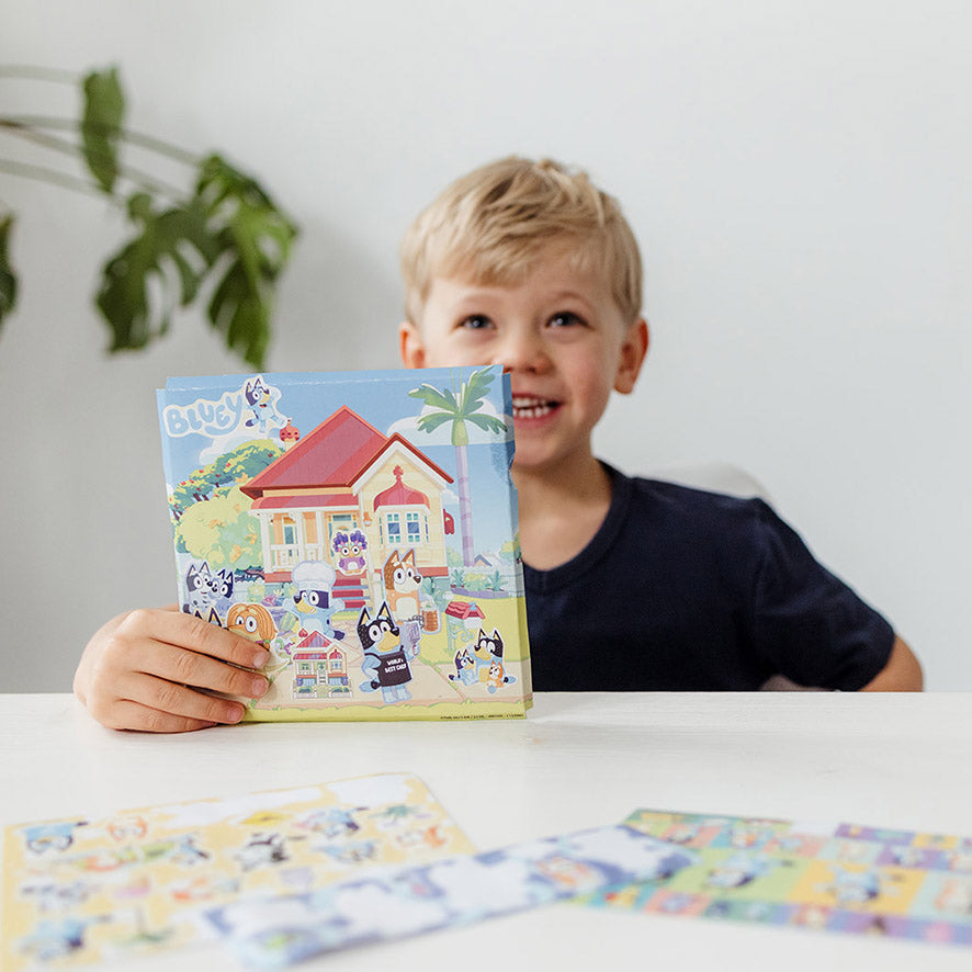 Rapaz sorridente a segurar uma folha de cenário da casa da Bluey, incentivando o jogo imaginativo.