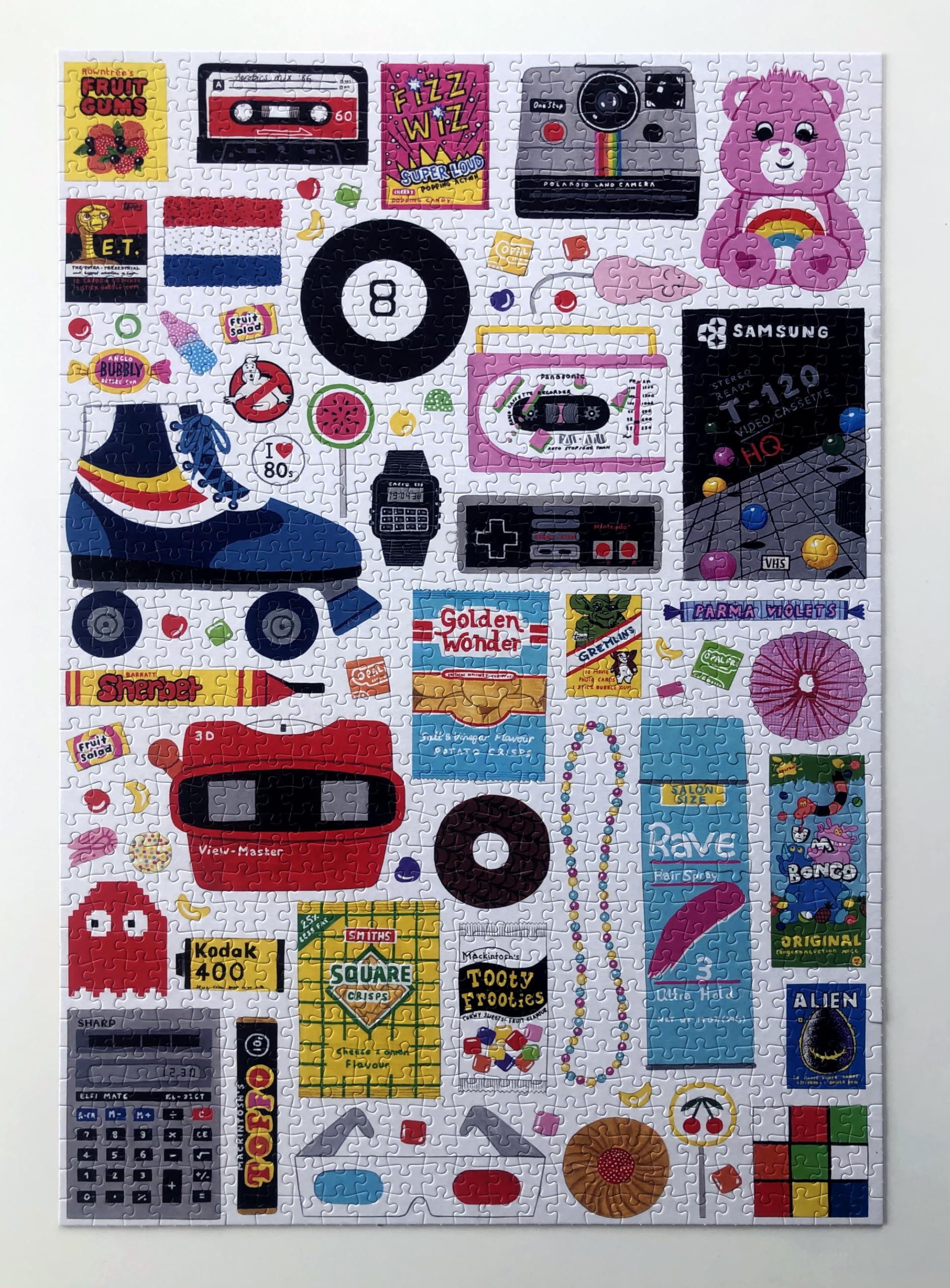 Puzzle Happily in the 80's de 1000 peças montado, exibindo a riqueza de detalhes e cores dos objetos icónicos da década de 80, como um Pac-Man, patins e uma cassete de música.