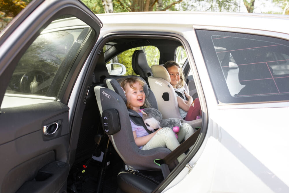 Duas crianças sentadas em cadeiras auto AXKID Minikid 4 instaladas na parte traseira de um carro.