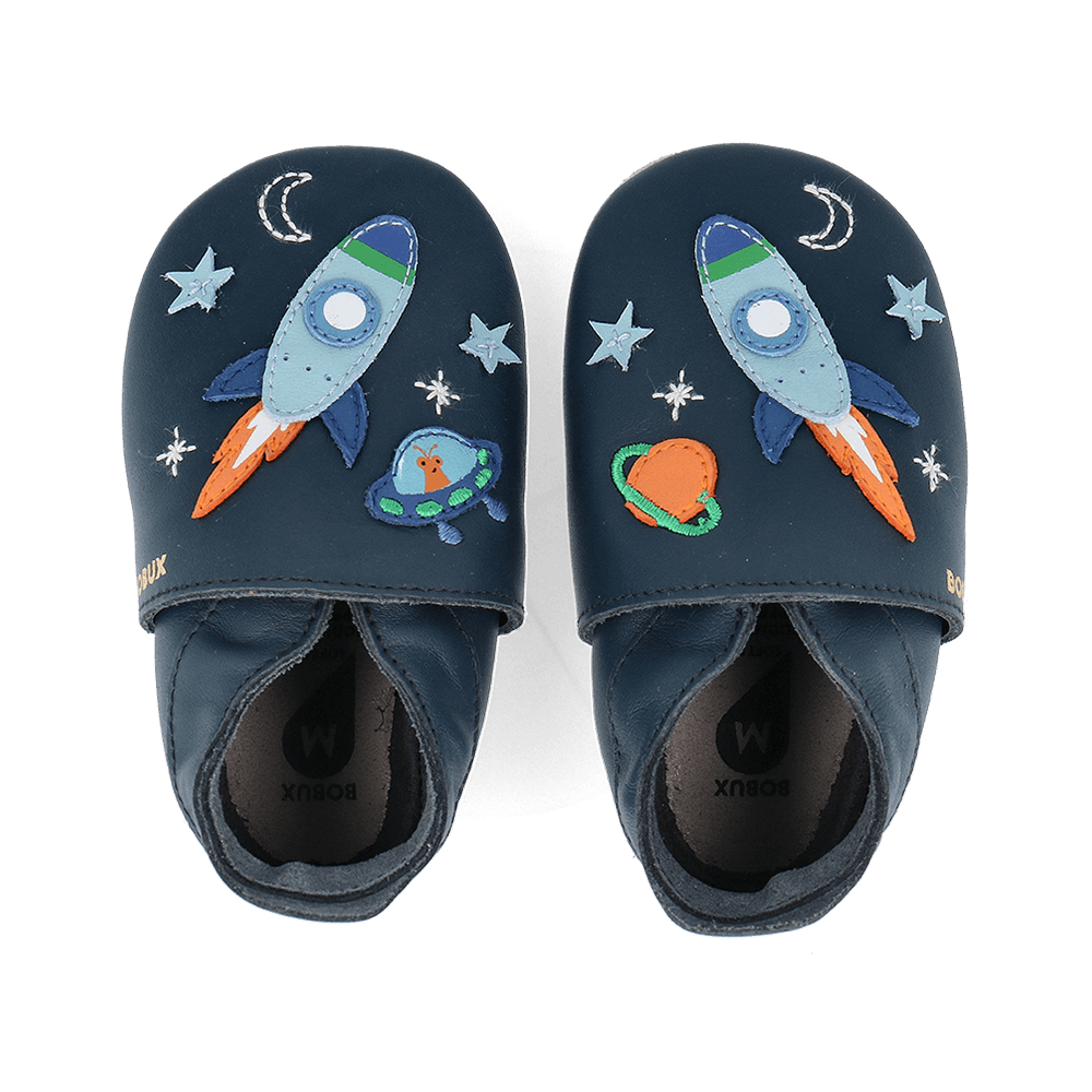 Par de sapatos Bobux Cosmic Rocket Soft Sole em azul-marinho, vistos de cima, com foguetões, estrelas e um OVNI bordados.