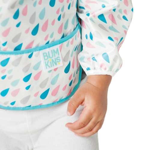 Detalhe de um bebé a usar o babete Bumkins, mostrando o encaixe da manga elástica e o bolso frontal com o logótipo da marca.