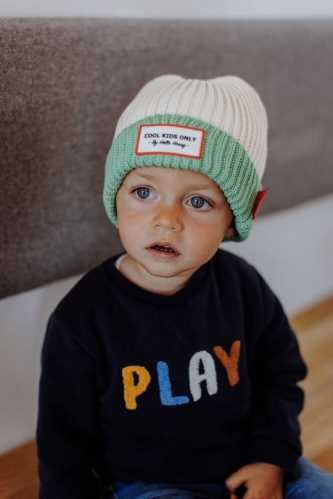 Bebé a usar o gorro HELLO HOSSY Grandma Green, mostrando o ajuste confortável e o estilo do gorro.