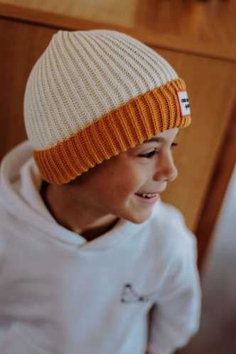 Criança de perfil a usar o gorro Hello Hossy Grandma Curry, destacando o design bicolor e a malha canelada.