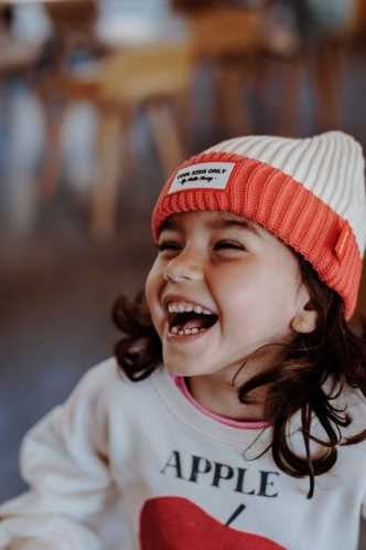 Criança sorridente a usar o gorro HELLO HOSSY Grandma Pink, destacando o conforto e o estilo vibrante do acessório.