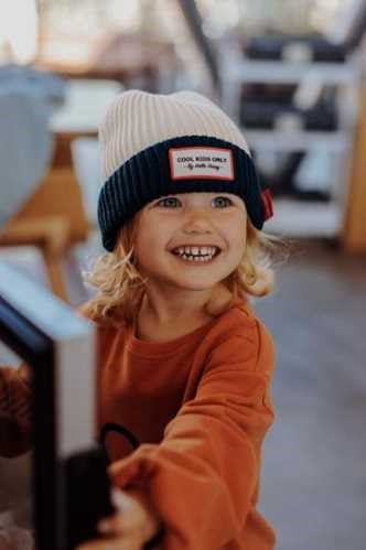Criança sorridente com cabelo louro a usar o gorro Hello Hossy Grandma Navy, mostrando o seu ajuste confortável e estilo.
