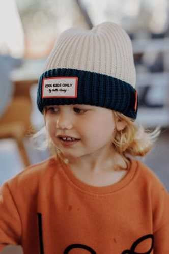 Criança com gorro Hello Hossy Grandma Navy, revelando o seu design bicolor creme e azul-marinho e o emblema "Cool Kids Only".