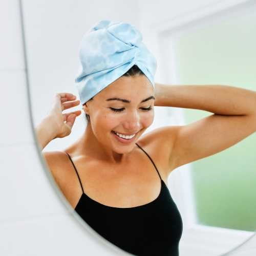 Mulher a ajustar a sua touca de secagem rápida Dock and Bay com padrão azul-claro em frente ao espelho da casa de banho.