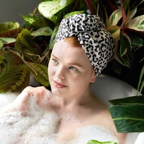 Mulher com cabelo ruivo a relaxar num banho de espuma, usando a touca de secagem rápida Dock and Bay com padrão de leopardo.
