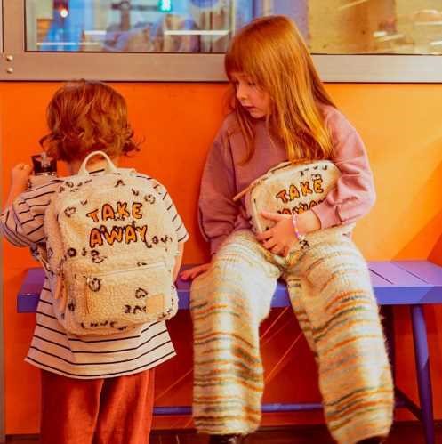 Duas crianças numa área com parede laranja; a criança mais nova usa a mochila Btbox TAKE AWAY e a mais velha segura uma bolsa a condizer.