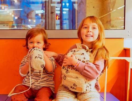 Criança mais nova a segurar uma bolsa a condizer e criança mais velha a usar a mochila Btbox TAKE AWAY, ambas sentadas num banco.