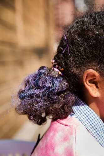 Cabelo escuro e encaracolado de criança com madeixas roxas e azuis, apanhado num rabo de cavalo.