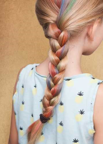 Trança de cabelo loiro infantil com madeixas de várias cores, criando um efeito arco-íris.