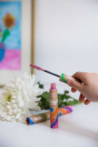 Mão a aplicar máscara de cabelo Namaki rosa, com o tubo e flores em fundo suave.