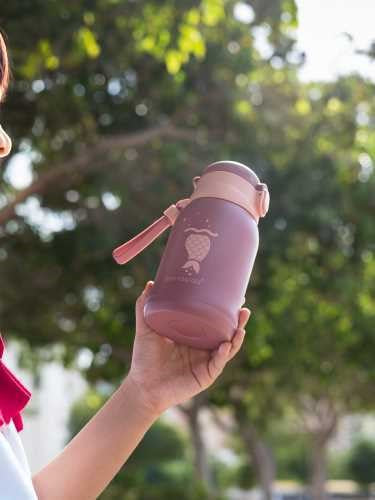 Mão de uma criança a segurar a garrafa Eco Rascals Inox 480ml rosa-claro com design de sereia, ao ar livre.