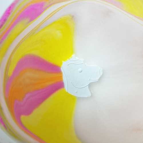 Vista aproximada da bomba de banho Zimpli Kids Unicórnio a dissolver-se na água, com cores vibrantes a espalhar-se e a figura branca do unicórnio visível.
