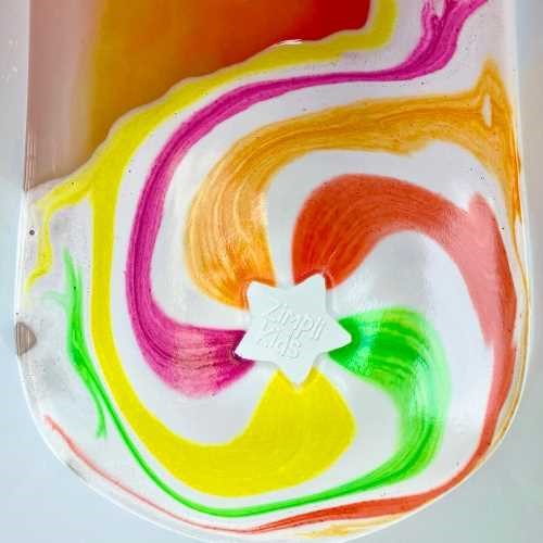 Detalhe da ZIMPLIKIDS Bomba de banho Estrela a dissolver-se na água, criando um efeito de cores arco-íris vibrante e lúdico.