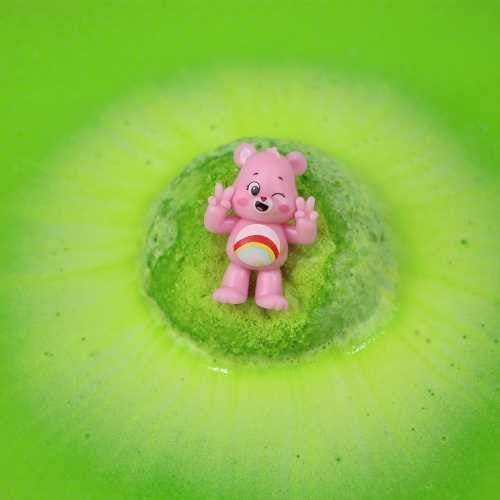 Figura rosa do Ursinho Carinhoso com arco-íris ao centro de uma bomba de banho verde efervescente.