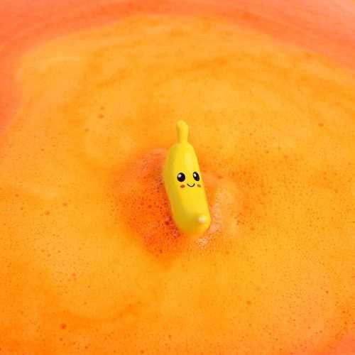 Figura de banana sorridente a flutuar na água laranja da banheira, após a dissolução da bomba.