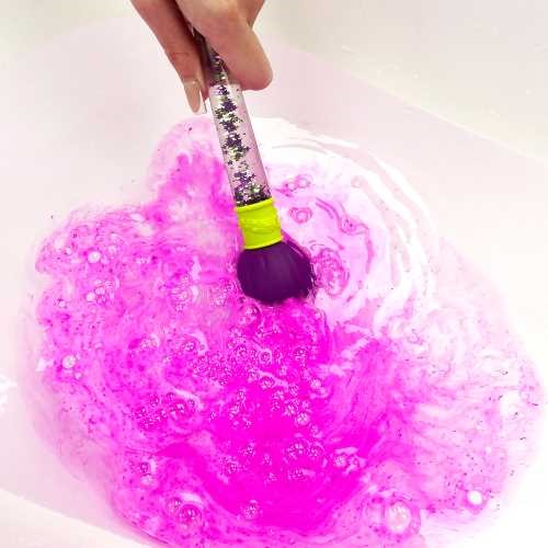 Pincel Mágico a criar um vibrante remoinho de cor rosa efervescente na água branca de uma banheira.