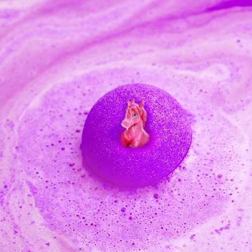 Figura de unicórnio rosa a emergir de uma bomba de banho roxa efervescente na água da banheira.